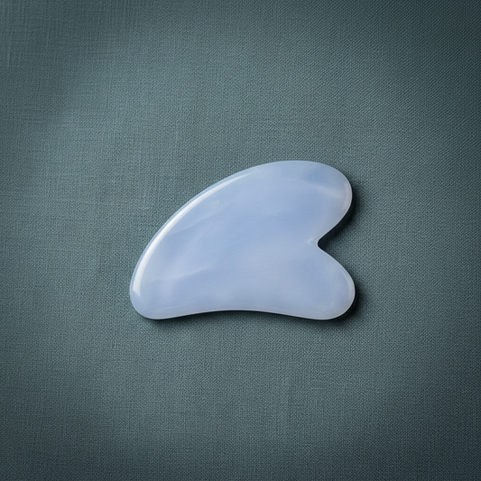 A blue chalcedony gua sha facial tool displayed on a muted teal linen background with soft natural lighting. — for Carpe Diem Dream