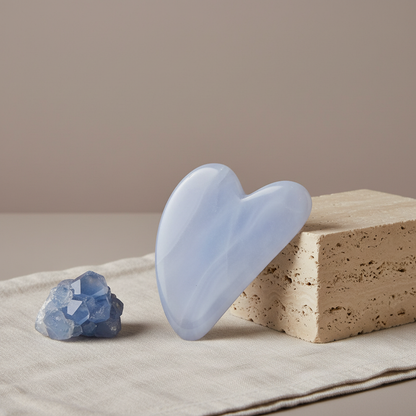 A blue chalcedony gua sha facial tool displayed on a soft neutral surface beside a natural stone block in gentle natural light. — for Carpe Diem Dream