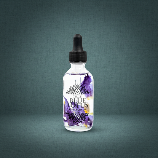 Blue Lotus Ritual Body Oil bottle with blue lotus petals and purple botanical design displayed on a muted teal linen background. — for Carpe Diem Dream