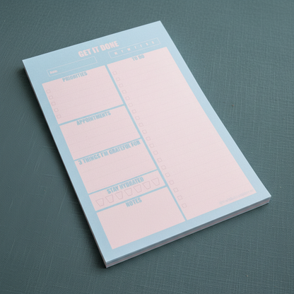 Angled close-up view of the blue and pink 7x10 daily planner notepad resting on muted teal fabric with soft natural shadow — for Carpe Diem Dream