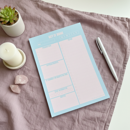 Blue and pink 7x10 daily planner notepad styled on blush fabric with a candle, succulent, and rose quartz crystals in soft natural light — for Carpe Diem Dream