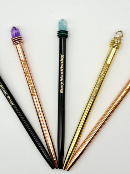 Set of metallic Busy Manifesting crystal mystic pens with faux crystal tops arranged in a fan layout on white background — for Carpe Diem Dream