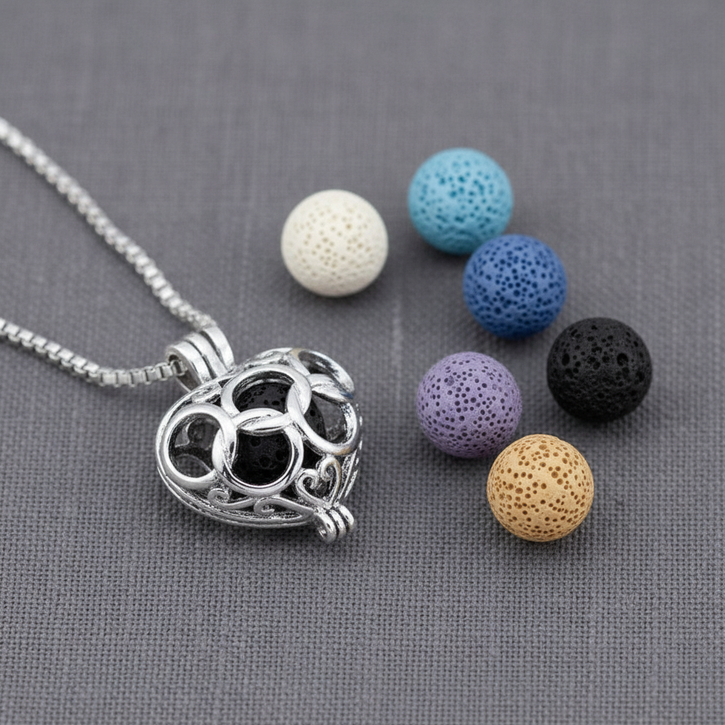 A silver heart-shaped cage diffuser necklace displayed with six interchangeable lava stone beads in assorted colors on a textured gray background. — for Carpe Diem Dream
