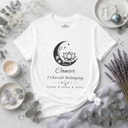 Cancer Moon I Cherish Belonging zodiac T-shirt in white with black moon-inspired lotus, floral, and celestial artwork and Sensitivity, Nurturing, Security text, styled in a bright cool-toned studio botanical flat lay with eucalyptus, lavender, crystals, and ceramic accents. — for Carpe Diem Dream