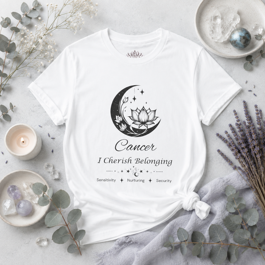 Cancer Moon I Cherish Belonging zodiac T-shirt in white with black moon-inspired lotus, floral, and celestial artwork and Sensitivity, Nurturing, Security text, styled in a bright cool-toned studio botanical flat lay with eucalyptus, lavender, crystals, and ceramic accents. — for Carpe Diem Dream
