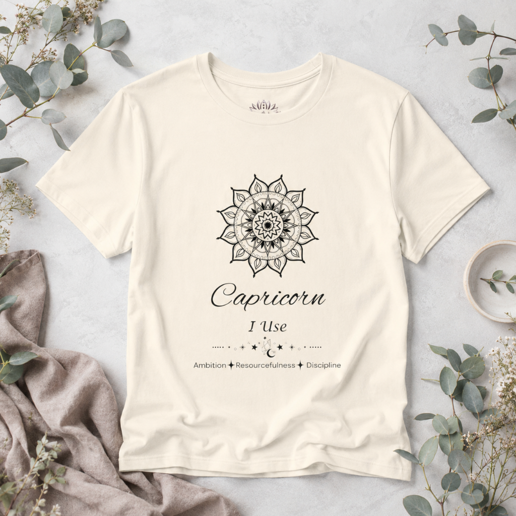 Capricorn Sun I Use zodiac T-shirt in natural with black sun-inspired mandala artwork and Ambition, Resourcefulness, Discipline text, styled in a cool-toned studio botanical flat lay. — for Carpe Diem Dream