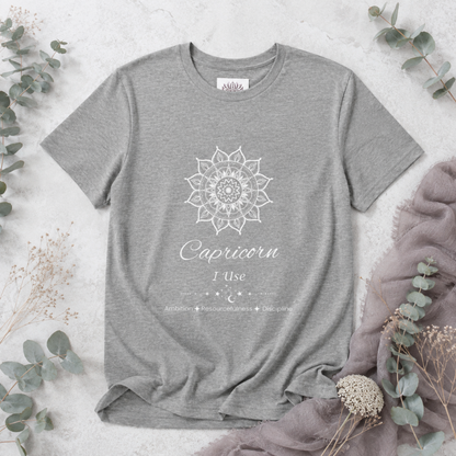 Capricorn Sun I Use zodiac t-shirt in athletic heather with white sun-inspired mandala artwork and Ambition, Resourcefulness, and Discipline text, shown in a soft botanical flat lay — for Carpe Diem Dream