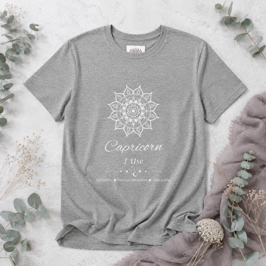 Capricorn Sun I Use zodiac t-shirt in athletic heather with white sun-inspired mandala artwork and Ambition, Resourcefulness, and Discipline text, shown in a soft botanical flat lay — for Carpe Diem Dream