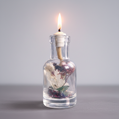 A Capricorn zodiac oil candle in a clear glass vessel with embedded botanicals burns with a steady flame on a soft neutral surface against a smooth light gray background. — for Carpe Diem Dream