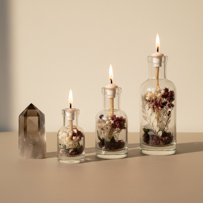 Three Capricorn zodiac oil candles in different sizes are displayed in clear glass vessels with embedded botanicals beside a crystal on a warm neutral background, showing size variation. — for Carpe Diem Dream
