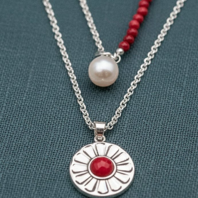 A close-up view of a layered necklace set featuring a red carnelian pendant necklace and a freshwater pearl choker displayed against a textured teal background. — for Carpe Diem Dream