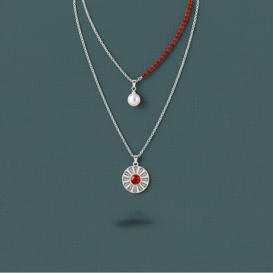 A layered necklace set featuring a red carnelian pendant necklace and a freshwater pearl choker displayed against a muted teal background. — for Carpe Diem Dream