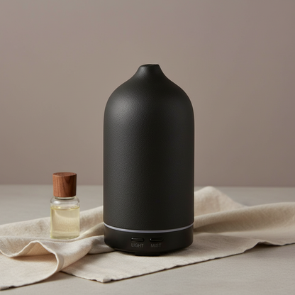 A matte black ceramic diffuser displayed on a neutral surface with a small essential oil bottle and soft fabric in clean, minimal lighting. — for Carpe Diem Dream