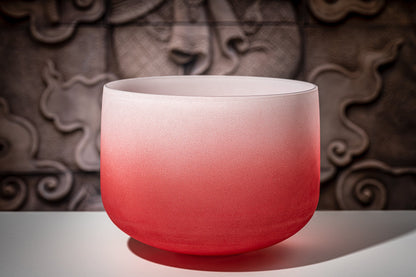 Red gradient frosted quartz crystal singing bowl representing the root chakra displayed on a white surface with decorative carved background — for Carpe Diem Dream
