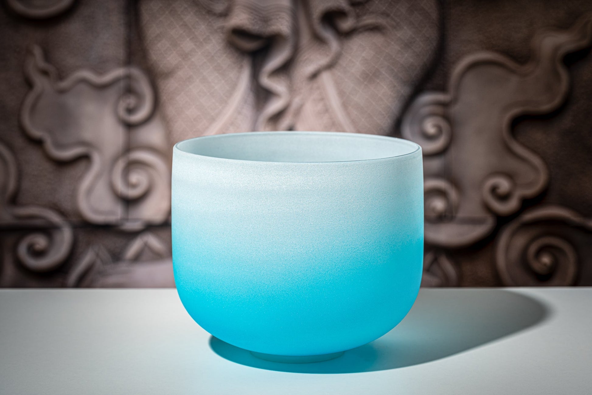 Blue gradient frosted quartz crystal singing bowl representing the throat chakra displayed on a white surface with decorative carved background — for Carpe Diem Dream