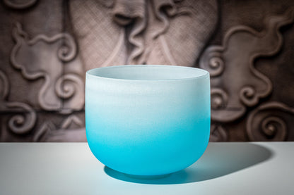 Blue gradient frosted quartz crystal singing bowl representing the throat chakra displayed on a white surface with decorative carved background — for Carpe Diem Dream