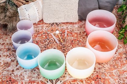 Seven gradient color frosted quartz crystal singing bowls arranged on a patterned rug with silicone rods and wooden mallet displayed — for Carpe Diem Dream