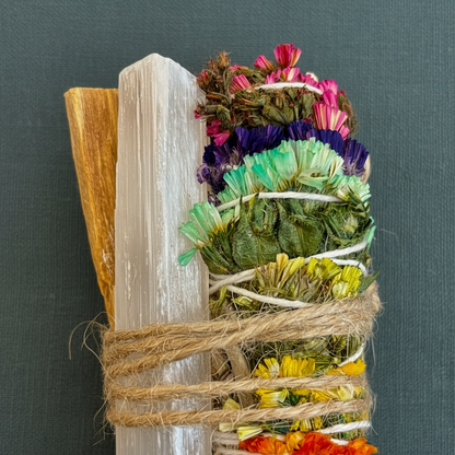 A close-up of a chakra sage smudge bundle tied with twine alongside a Palo Santo stick and a raw selenite wand against a muted teal background. — for Carpe Diem Dream