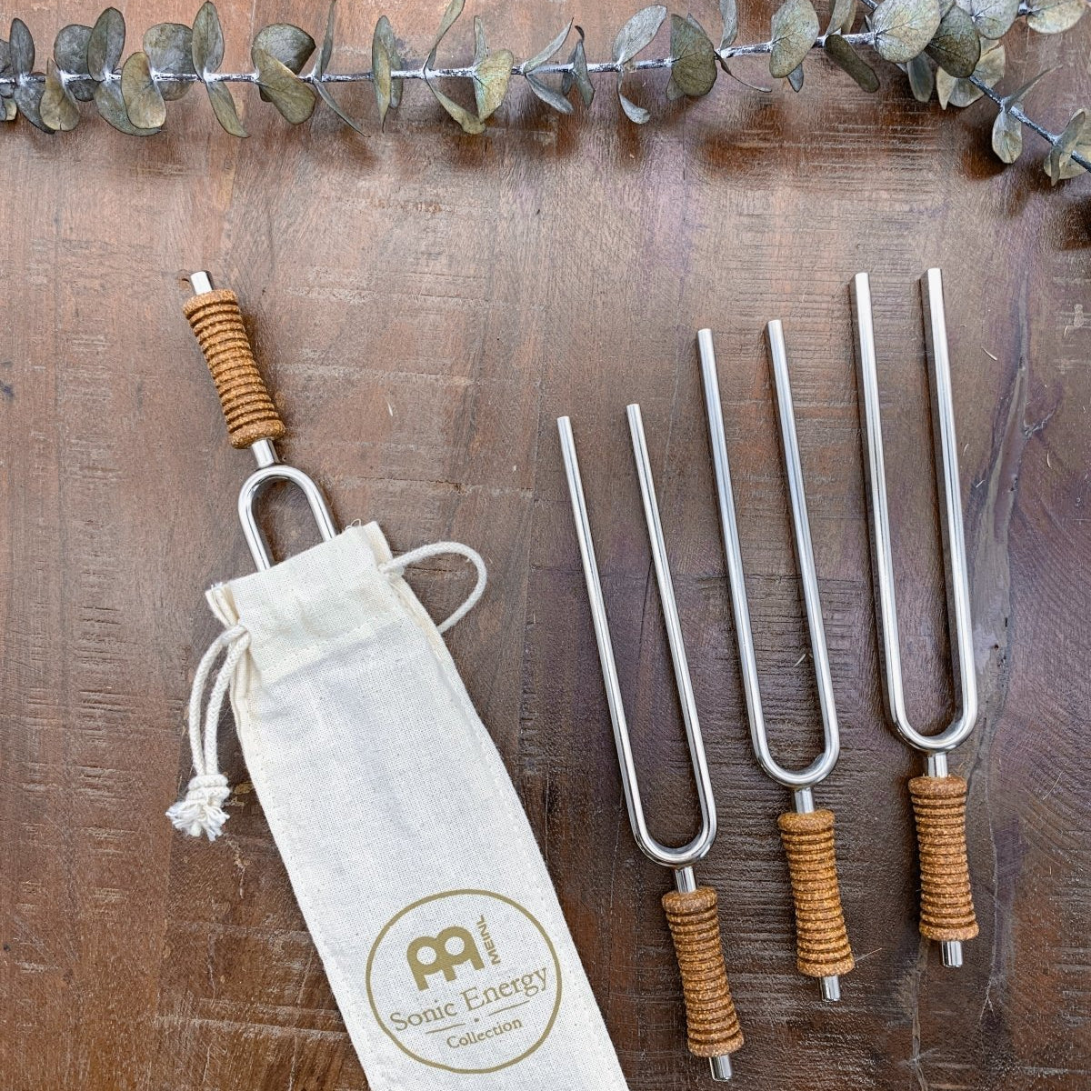 Multiple metal tuning forks with cork handles arranged beside a cotton storage pouch on a wooden surface. — for Carpe Diem Dream
