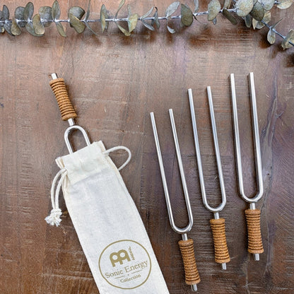 Multiple metal tuning forks with cork handles arranged beside a cotton storage pouch on a wooden surface. — for Carpe Diem Dream