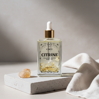 Citrine Ritual Body Oil glass dropper bottle displayed on a travertine pedestal with a citrine crystal beside it. — for Carpe Diem Dream