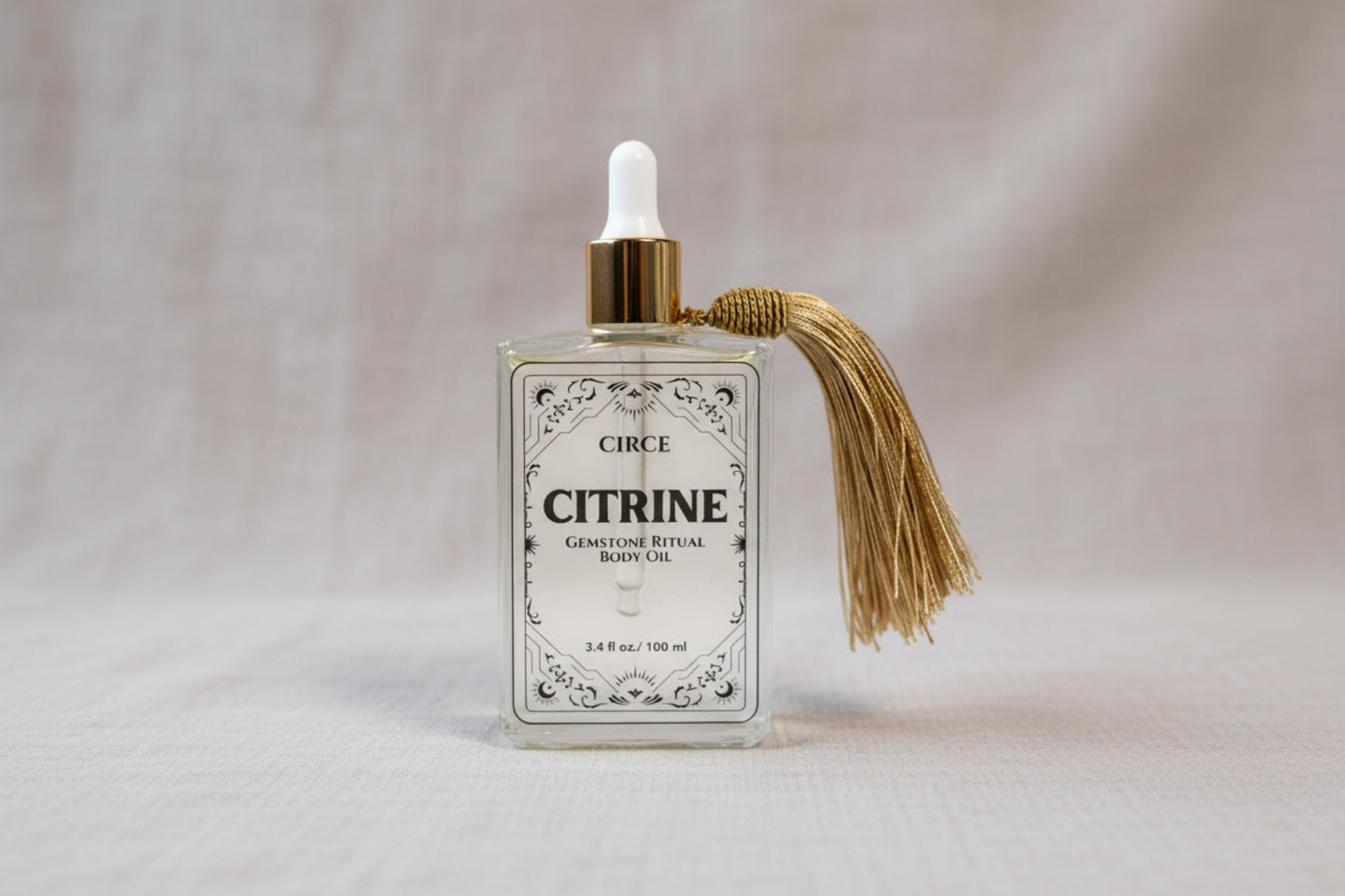 Citrine Ritual Body Oil glass dropper bottle with gold tassel displayed on a soft neutral linen background. — for Carpe Diem Dream