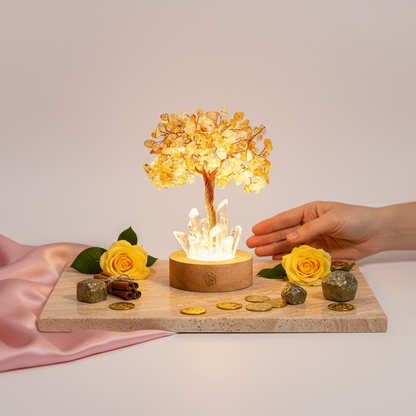 Golden citrine gemstone tree lamp on stone platform with yellow roses, gold coins, and a hand placing a green quartz cluster on mauve backdrop. — for Carpe Diem Dream