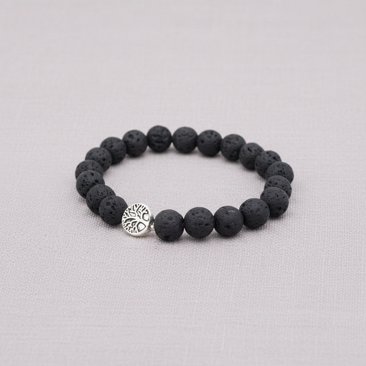 A black lava stone stretch bracelet with a silver Tree of Life charm displayed on a textured linen background. — for Carpe Diem Dream