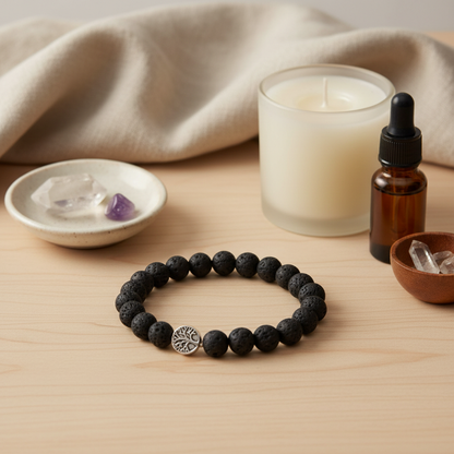A black lava stone stretch bracelet with a silver Tree of Life charm displayed on a wooden surface beside a candle, an amber essential oil bottle, and small crystals. — for Carpe Diem Dream