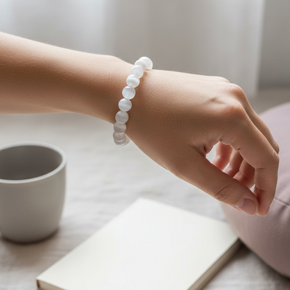 Hand wearing a Selenite cleansing bracelet in soft morning light above a journal and cup on a neutral table. — for Carpe Diem Dream