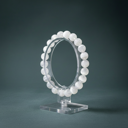 Selenite cleansing bracelet displayed upright on a clear stand against a muted teal backdrop. — for Carpe Diem Dream
