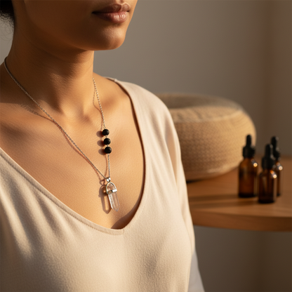 A clear crystal pendant necklace with black lava stone beads worn on a silver chain with amber essential oil bottles in the background. — for Carpe Diem Dream