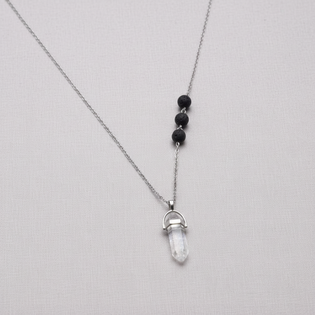 A clear crystal pendant necklace with black lava stone beads suspended on a silver chain against a textured linen background. — for Carpe Diem Dream