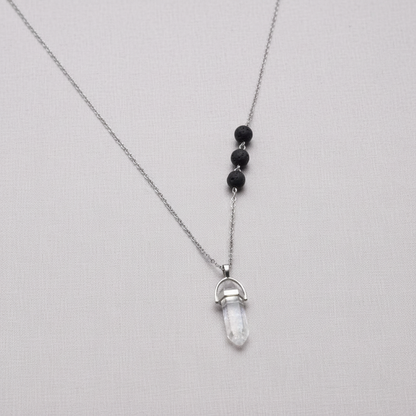 A clear crystal pendant necklace with black lava stone beads suspended on a silver chain against a textured linen background. — for Carpe Diem Dream