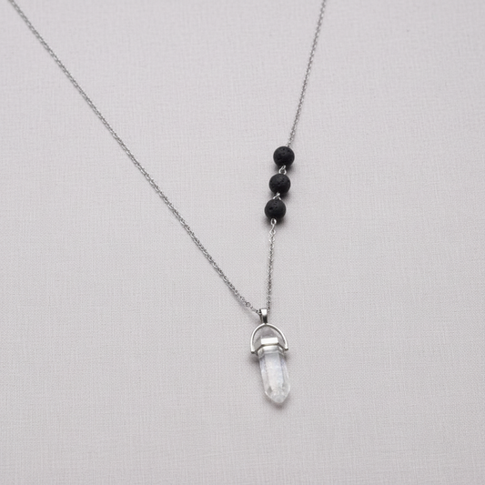 A clear crystal pendant necklace with black lava stone beads suspended on a silver chain against a textured linen background. — for Carpe Diem Dream