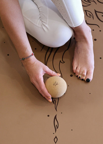 Hand holding large cork yoga massage ball on a yoga mat during a wellness recovery session. — for Carpe Diem Dream