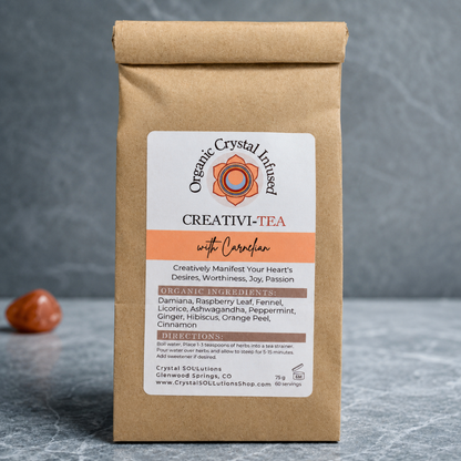 Creativi-Tea – Organic Crystal-Infused Herbal Tea with Carnelian photographed on a cool blue-gray stone surface with a softly textured blue-gray backdrop, cool diffused daylight, soft contact shadows, and premium commercial styling. The authentic product remains the focal point with a subtle Carnelian accent. — for Carpe Diem Dream
