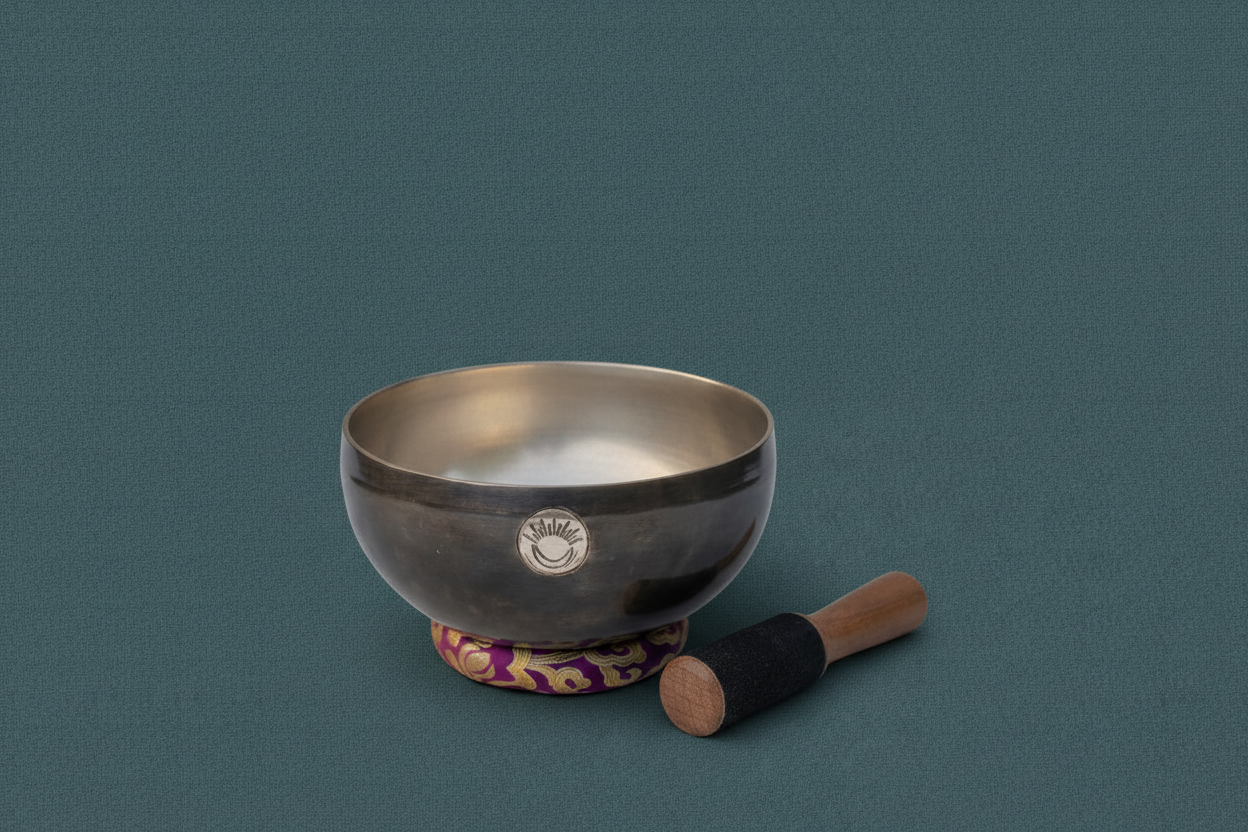 Hand-hammered Crown Chakra New Moon singing bowl tuned to B note resting on a purple cushion with wooden mallet on a muted teal linen background. — for Carpe Diem Dream