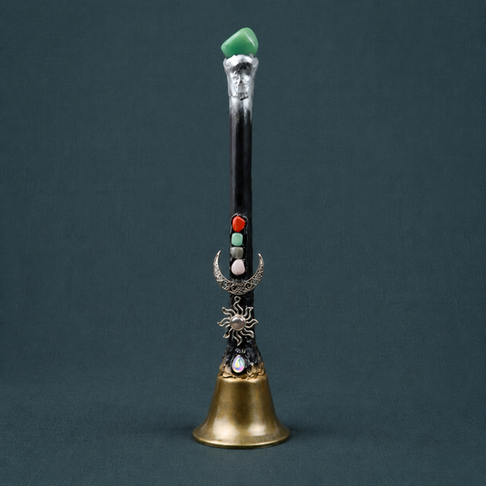 Green Aventurine crystal charm altar bell with a black handle, silver-tone moon and sun charms, and an antique gold-tone bell on dark teal textured linen. — for Carpe Diem Dream.