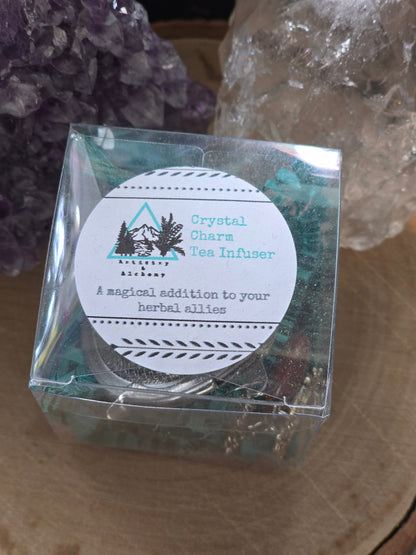 Crystal Charm Tea Infuser – Authentic supplier image showing the packaged tea infuser with crystal charms in a clear display box, styled in front of amethyst and clear quartz crystals on a natural wood surface. — for Carpe Diem Dream