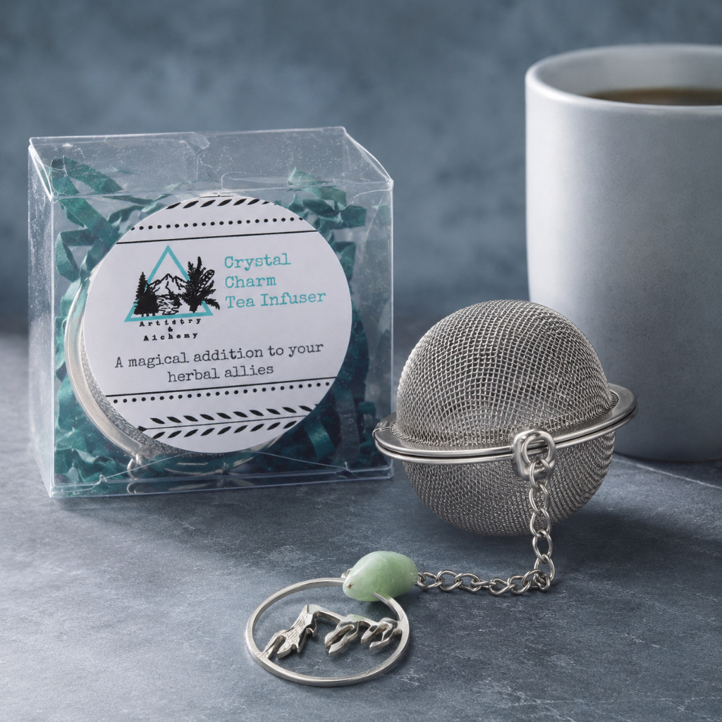 Crystal Charm Tea Infuser – authentic tea infuser photographed on a cool blue-gray stone surface with its clear display packaging, metal mesh strainer, chain, crystal charm, and soft ceramic mug accent. The product remains the focal point in a refined CDD editorial studio setting with cool diffused daylight. — for Carpe Diem Dream