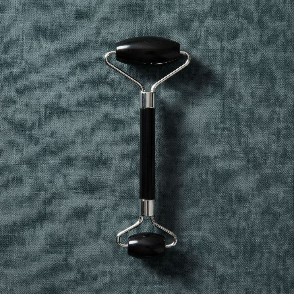 A black crystal face roller with dual rolling stones and a metal handle displayed upright on a muted teal linen background with soft lighting. — for Carpe Diem Dream