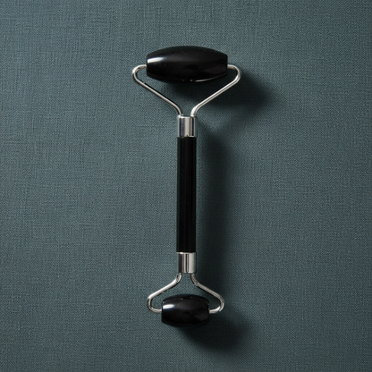 A black crystal face roller with dual rolling stones and a metal handle displayed upright on a muted teal linen background with soft lighting. — for Carpe Diem Dream
