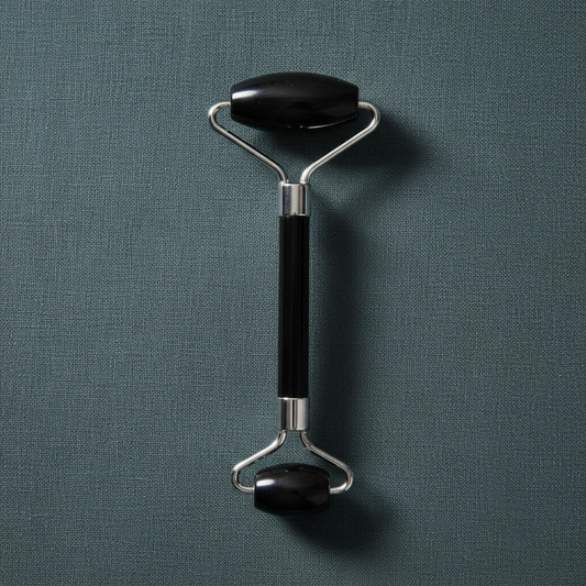 A black crystal face roller with dual rolling stones and a metal handle displayed upright on a muted teal linen background with soft lighting. — for Carpe Diem Dream