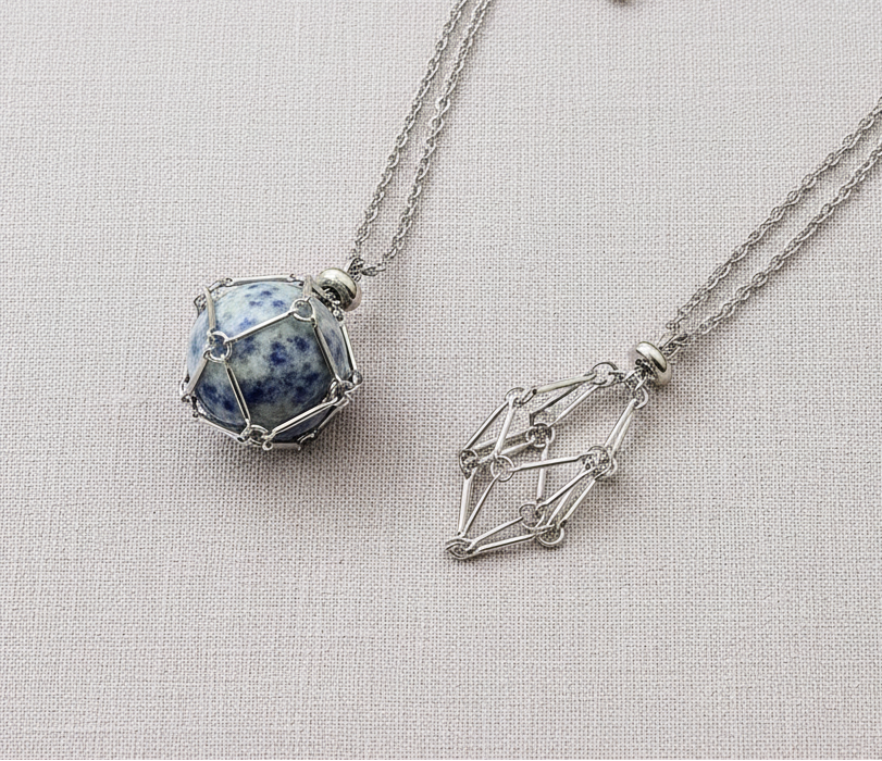 A crystal gem holder necklace with a blue stone in a silver wire cage displayed on a neutral textured background. — for Carpe Diem Dream

