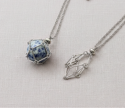 A crystal gem holder necklace with a blue stone in a silver wire cage displayed on a neutral textured background. — for Carpe Diem Dream
