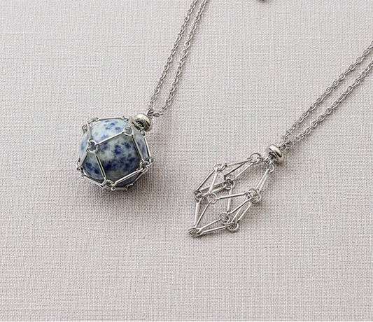 A crystal gem holder necklace with a blue stone in a silver wire cage displayed on a neutral textured background. — for Carpe Diem Dream
