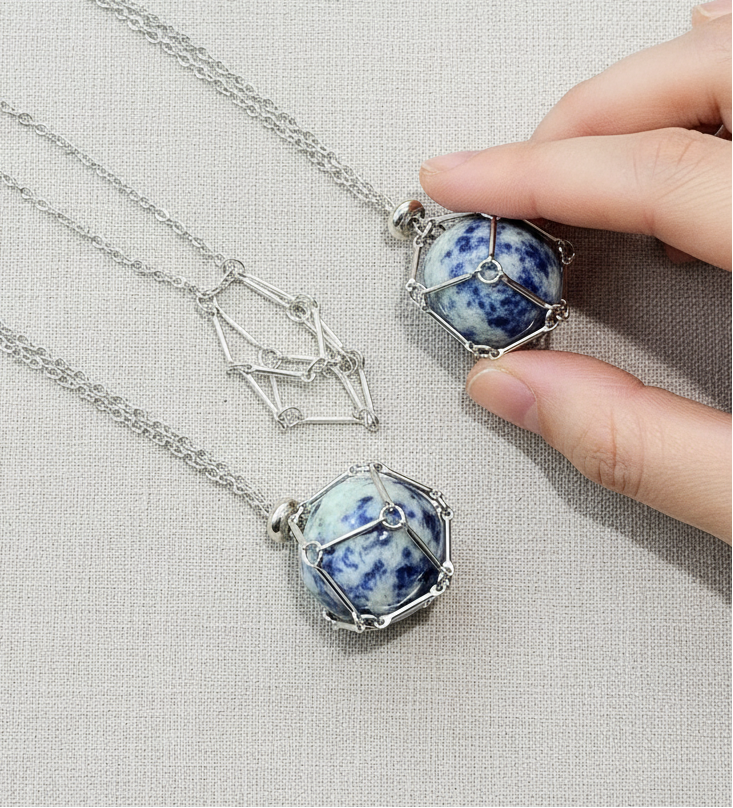 A crystal gem holder necklace with a blue stone in a silver wire cage held by a hand on a neutral textured background. — for Carpe Diem Dream
