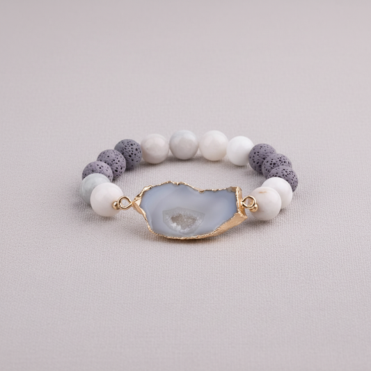 A crystal and gold lava stone stretch bracelet featuring a gold-edged center stone and porous lava beads displayed on a textured linen background. — for Carpe Diem Dream