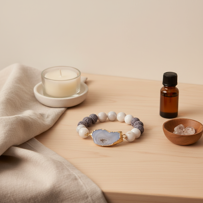 A crystal and gold lava stone stretch bracelet displayed on a wooden surface beside a candle, an amber essential oil bottle, and small crystals. — for Carpe Diem Dream